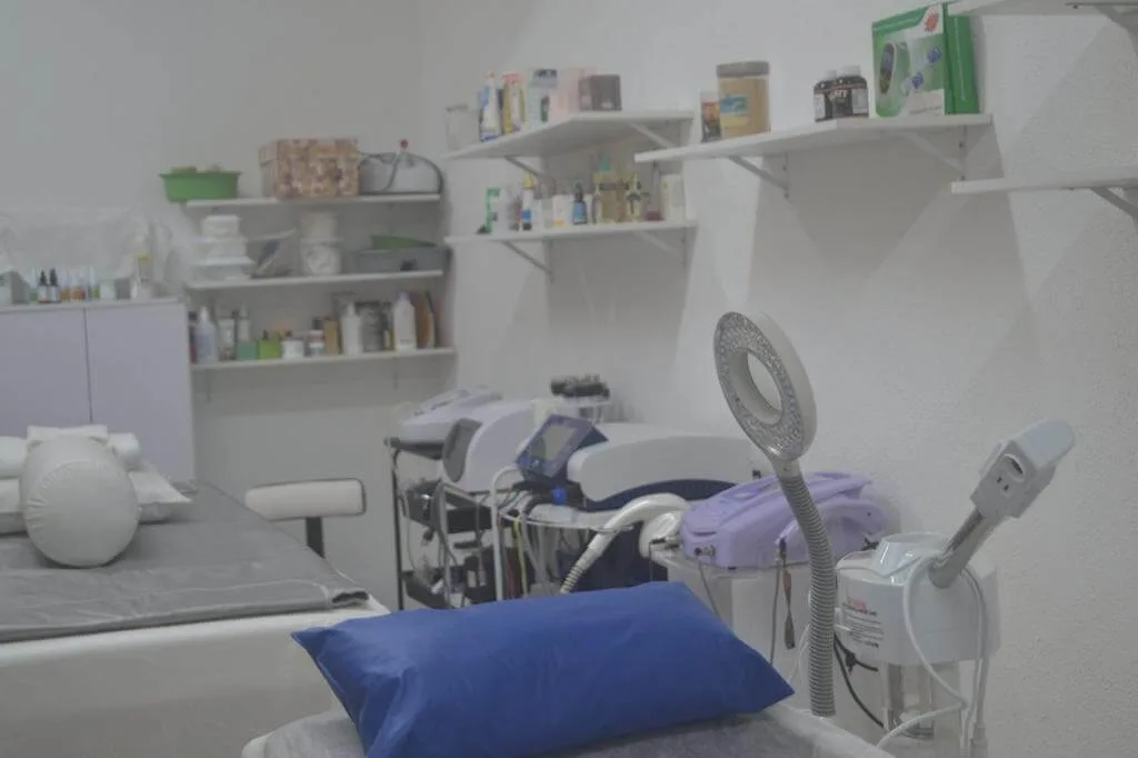 Sala de atendimento com maca, aparelhos e prateleiras brancas com frascos