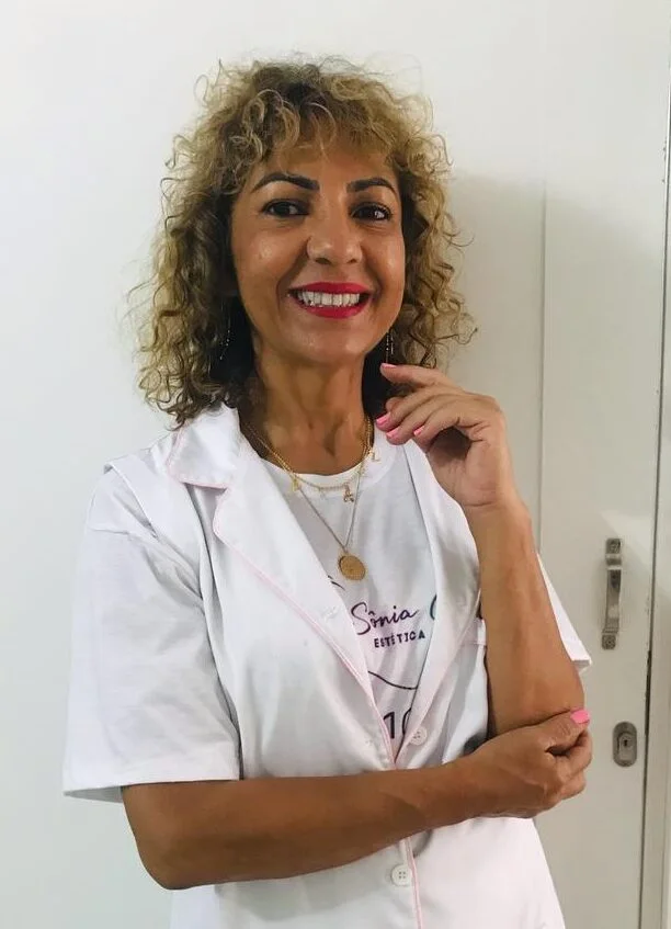 Sônia Garcia de jaleco branco, sorrindo, com a mão no queixo